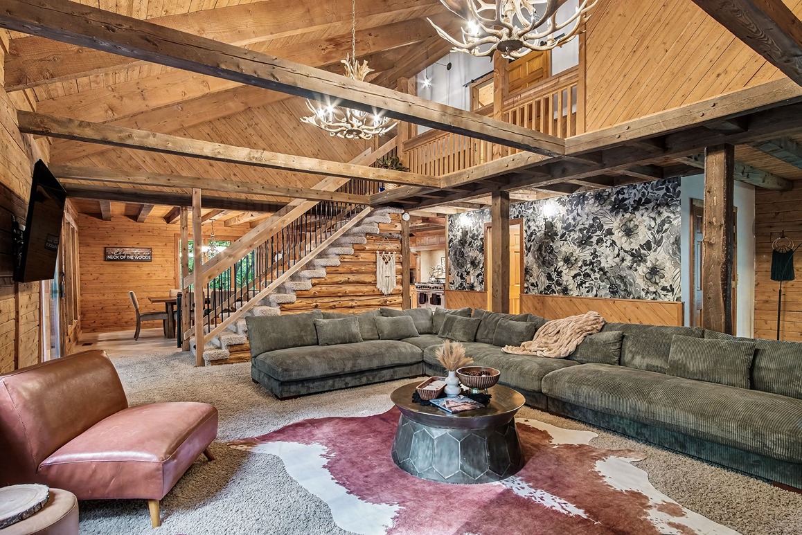 Open great room with sectional seating, staircase, and exposed wood beams